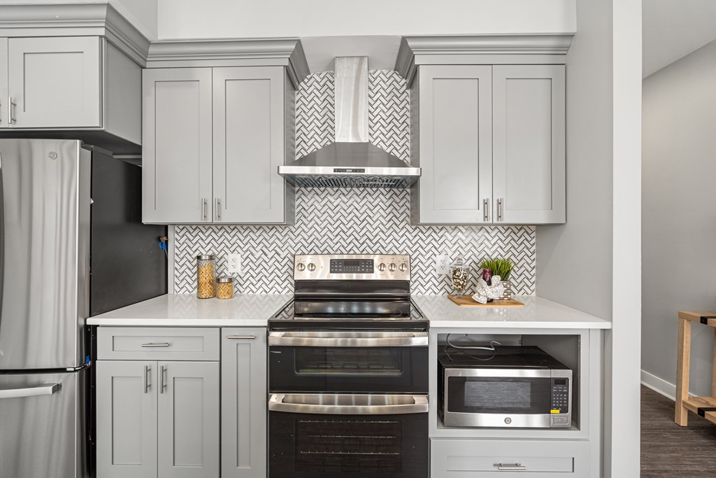 A kitchen with white cabinets and a black and white tiled backsplash.