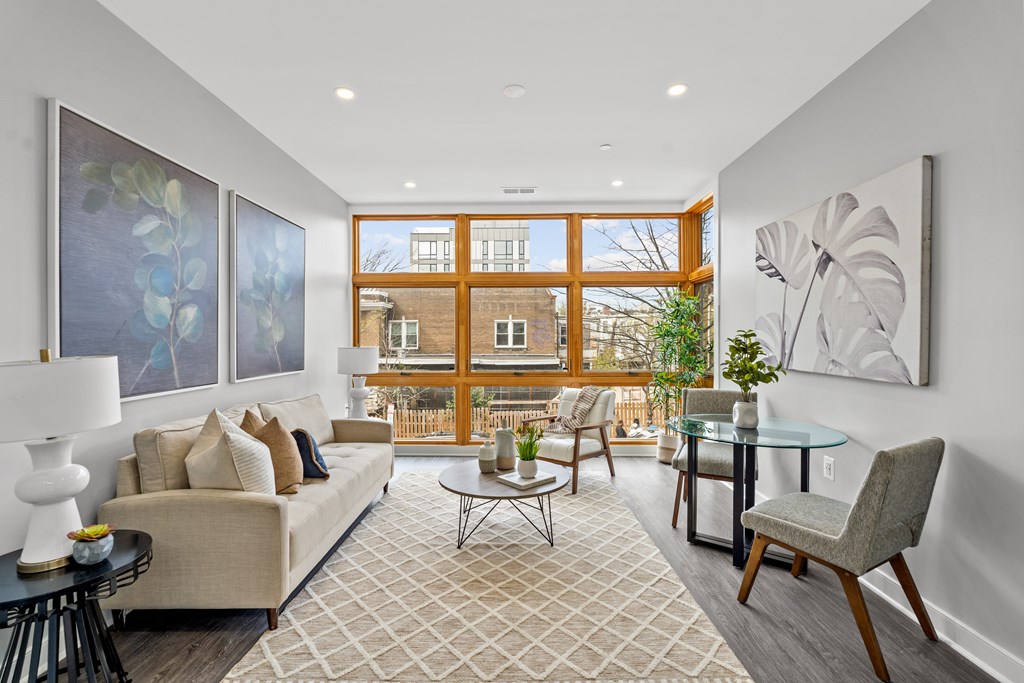 A well-lit living room with a large window, a sofa, a coffee table, and a painting on the wall.