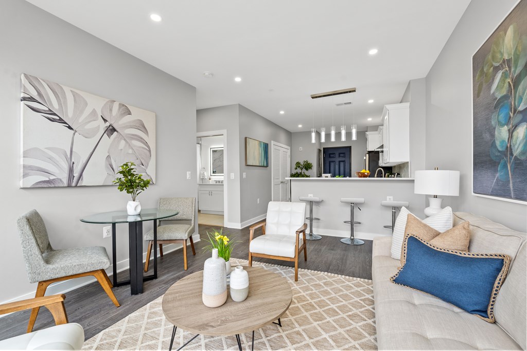 A modern living room with a grey couch, a glass table, and a painting on the wall.
