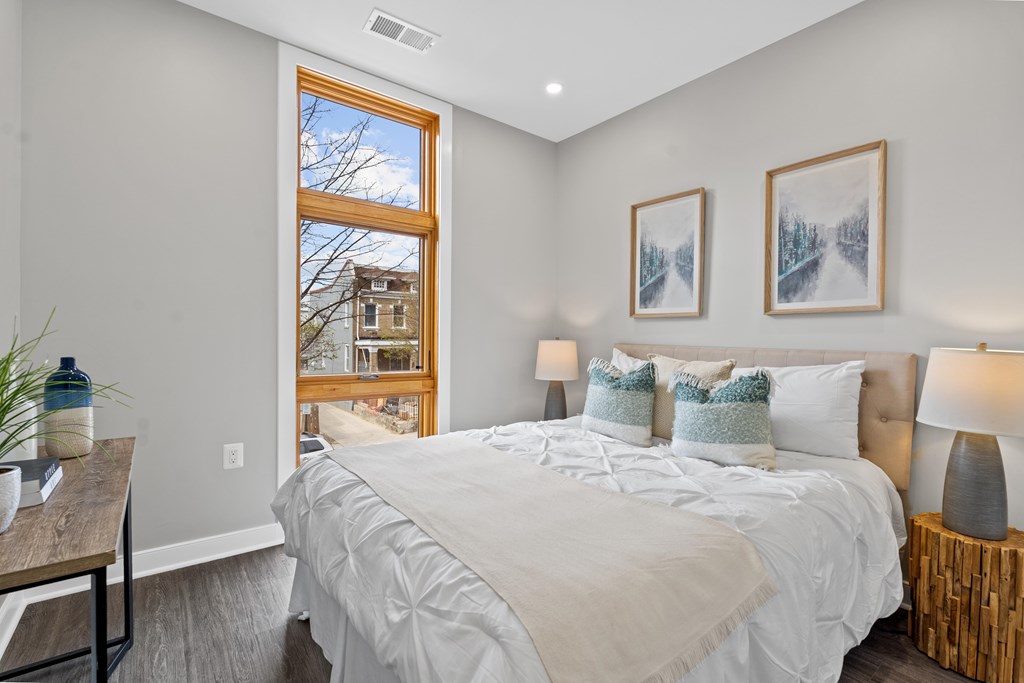 A bedroom with a large bed and a view of a house through a window.