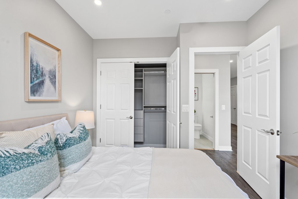 A bedroom with a bed, a painting, and a door leading to a bathroom.