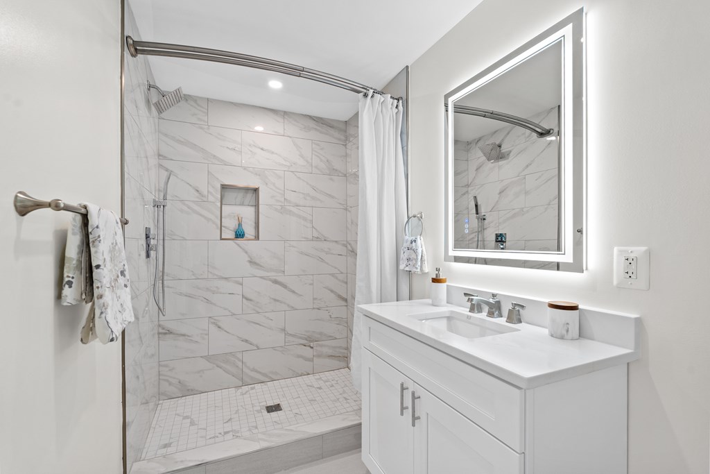 A white bathroom with a marble shower and a white sink.