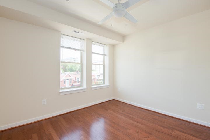 an empty room with two windows and a ceiling fan