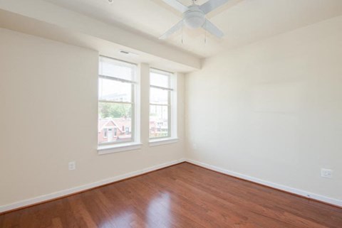 an empty room with two windows and a ceiling fan