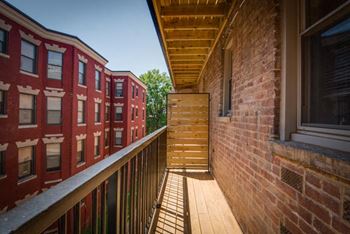 a balcony with a wooden railing and a brick building in the background