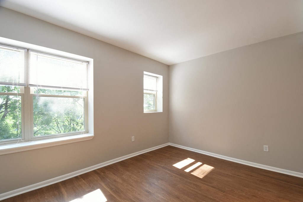 an empty bedroom with a large window and hardwood floors