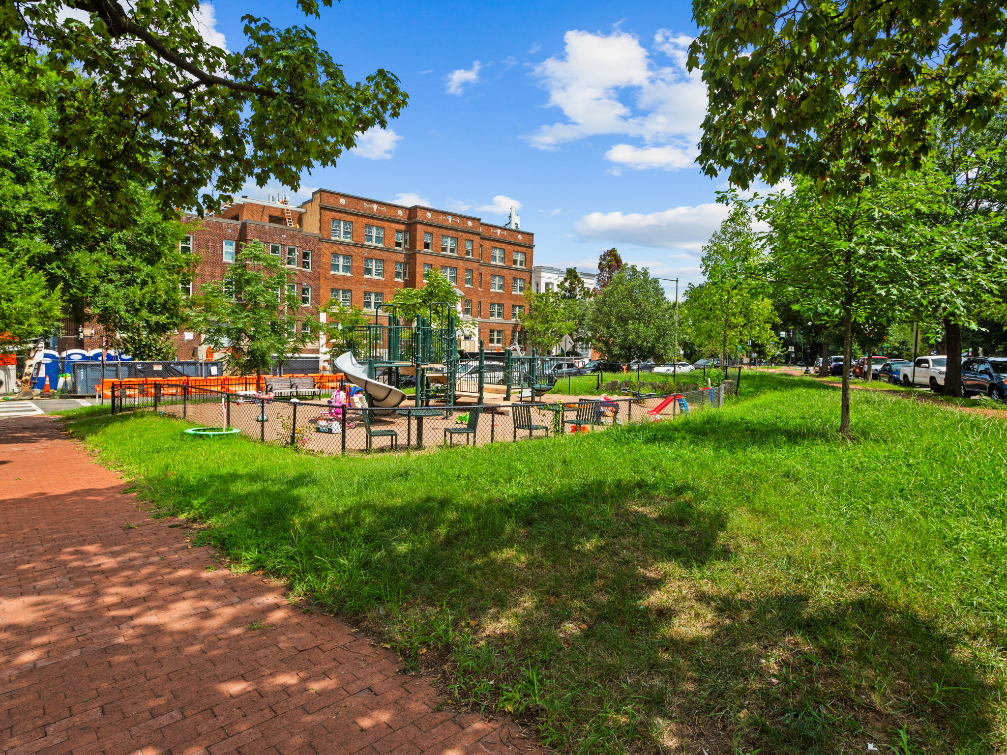 A park with a red brick pathway and green grass.
