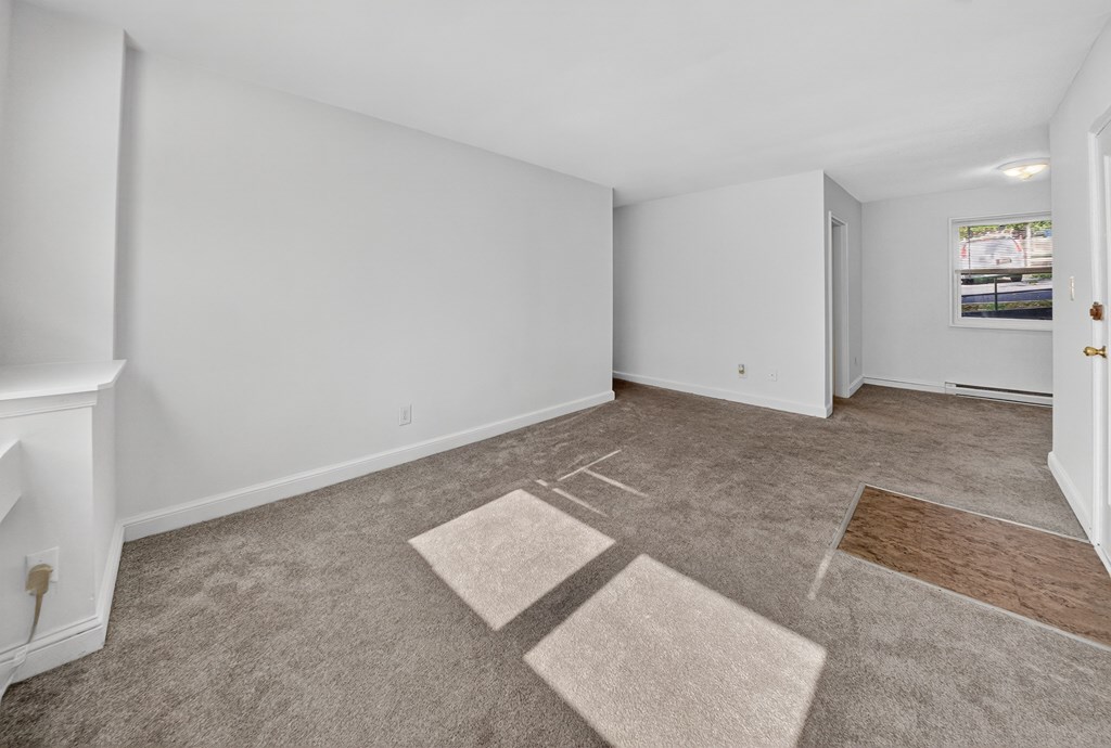 A room with a carpeted floor and a fireplace on the left side.