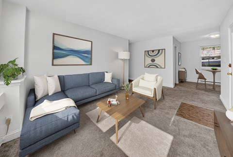A living room with a blue couch, a white chair, and a painting on the wall.