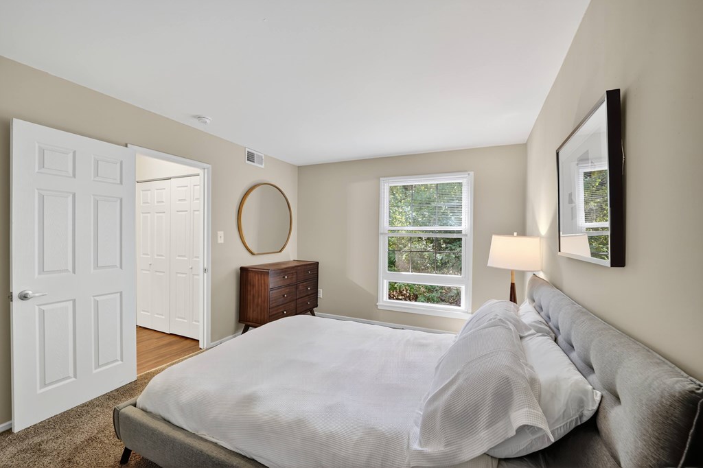 A bedroom with a large bed and a window overlooking a tree-filled yard.