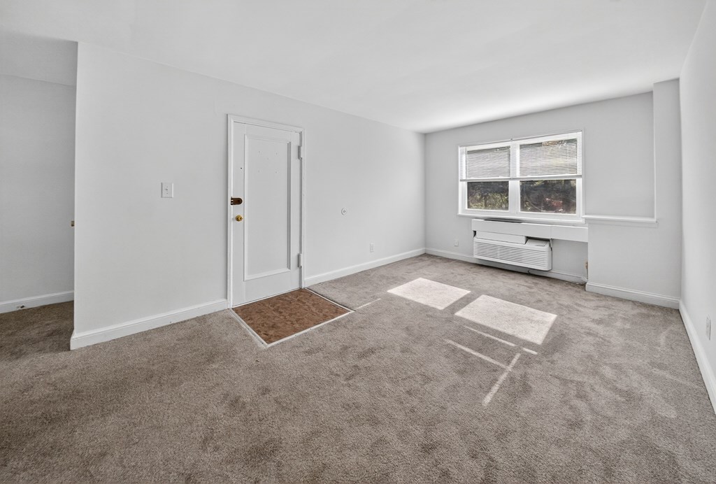 A room with a carpet, a door, a window with a view of trees and a small table.
