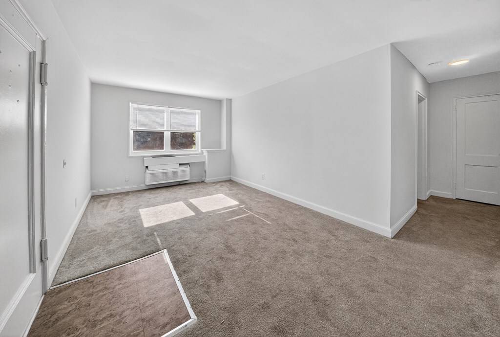 A room with a carpeted floor and a window with blinds.