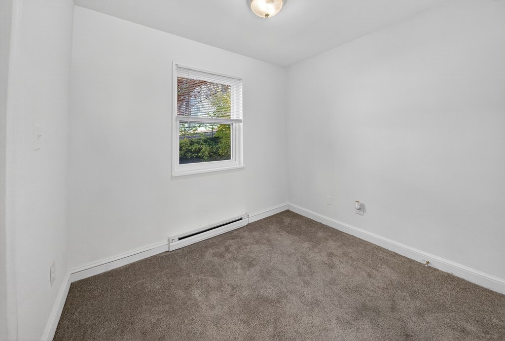 A room with a carpeted floor and a window showing a view of trees and a house.