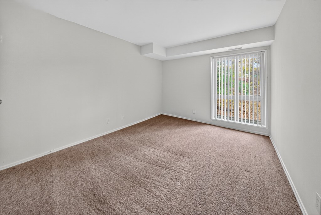 A room with a carpeted floor and a window with blinds.