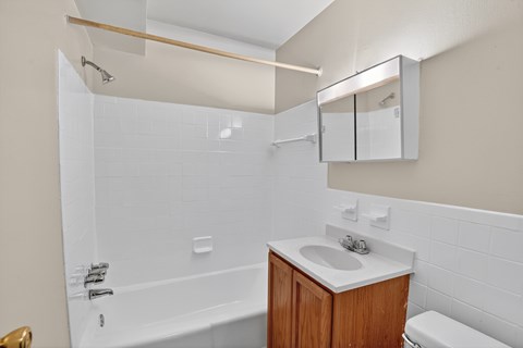 A white bathroom with a wooden vanity and a white toilet.