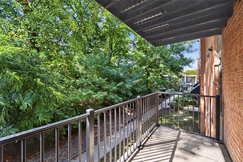 A balcony with a metal railing and a view of a green tree.