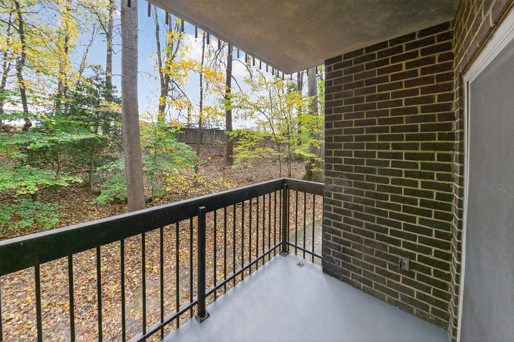 A balcony with a black railing and a view of trees and a hill.