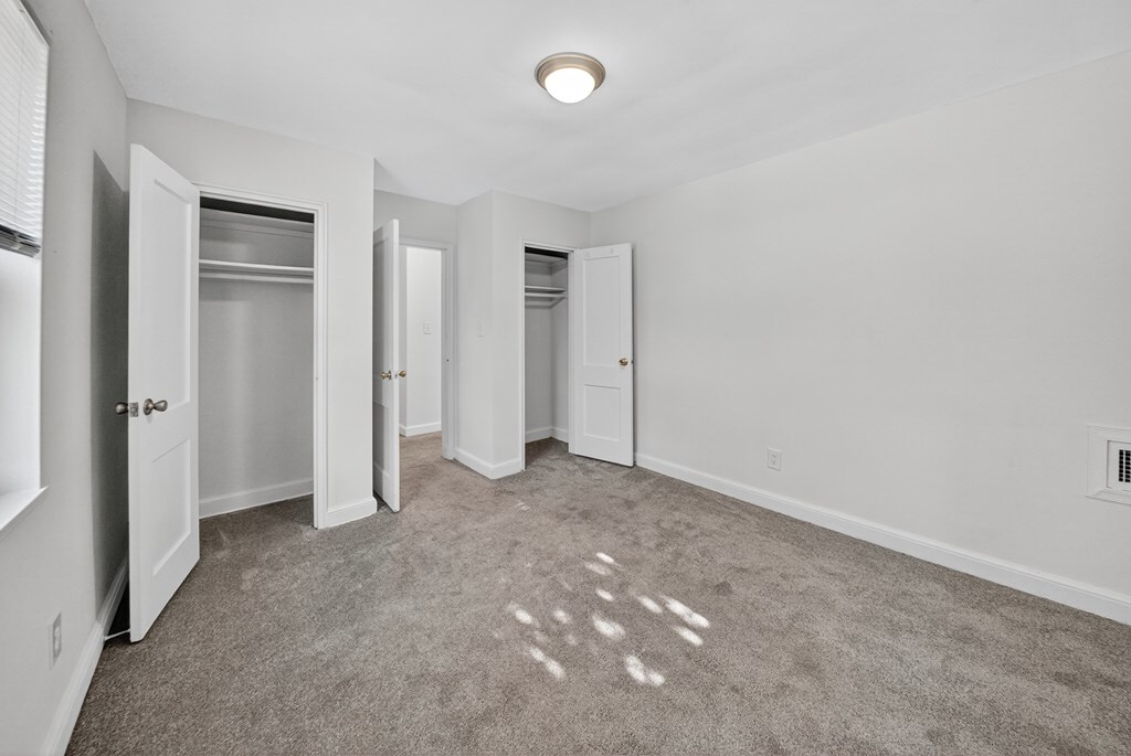 A room with white walls and a carpeted floor with a few stains.