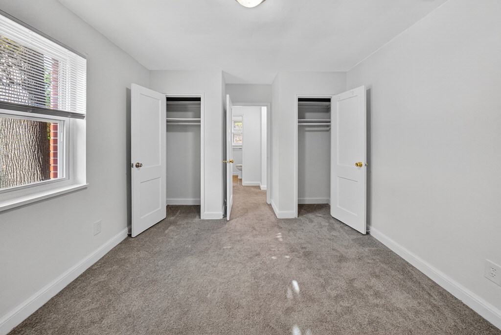A white room with a carpeted floor and a window with blinds.