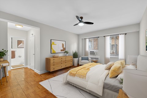 A bedroom with a bed, a couch, a ceiling fan, and a wooden dresser.