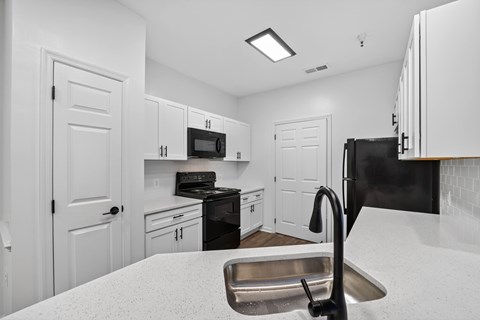 A kitchen with white cabinets and a black refrigerator.