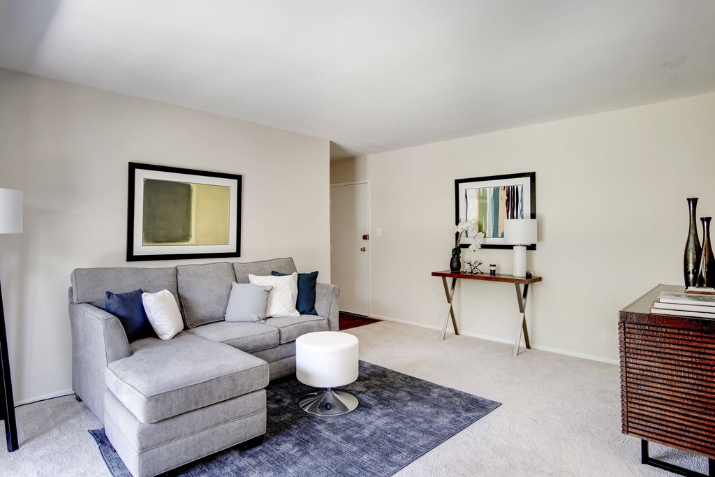 A grey couch with a white ottoman in front of a painting.