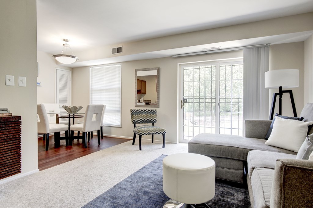 A well-lit living room with a grey couch and a white ottoman.