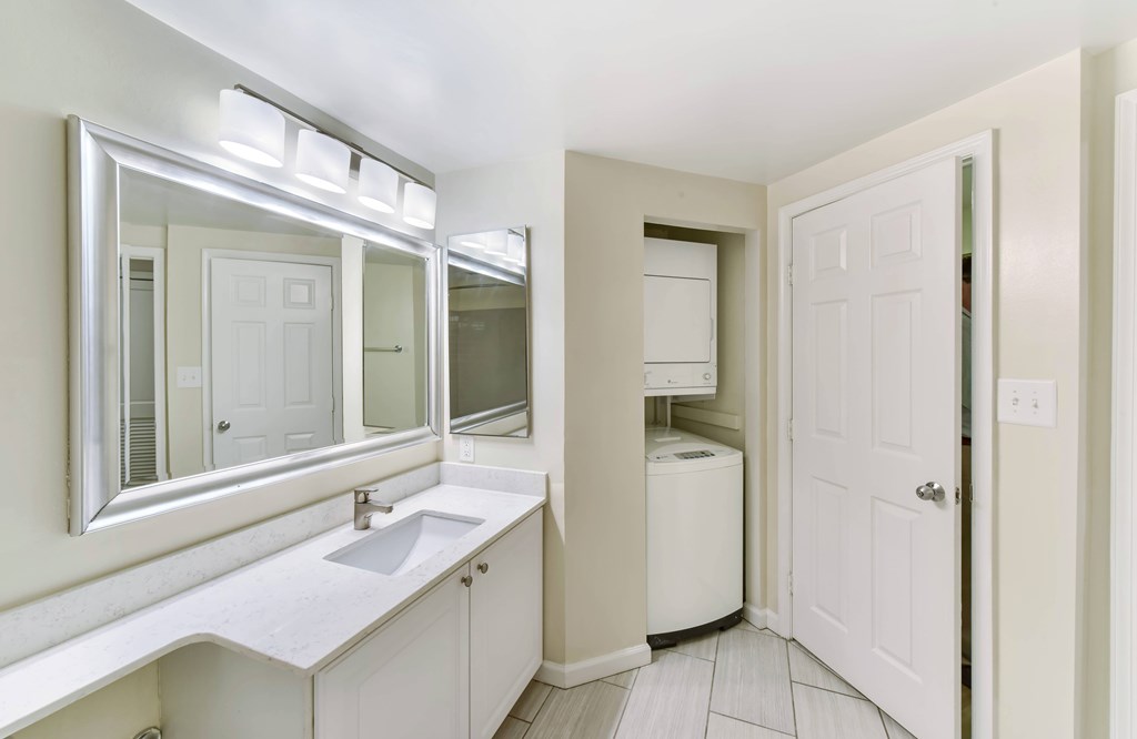 A white bathroom with a sink, mirror, and a white door.