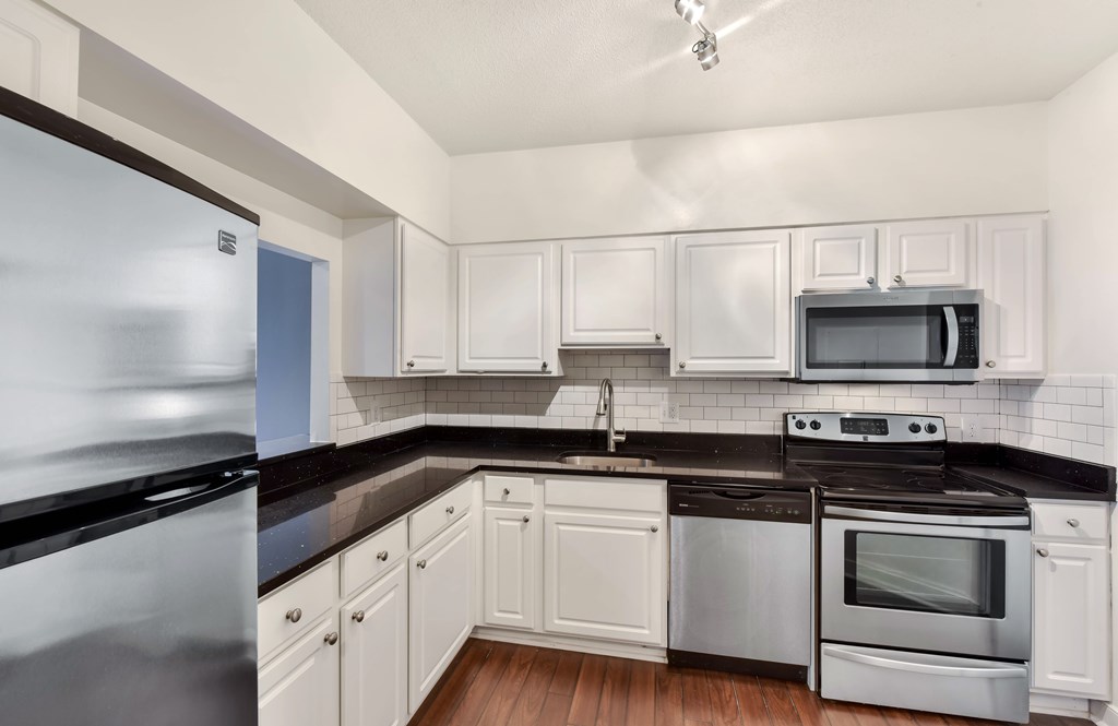 A kitchen with white cabinets and black countertops.