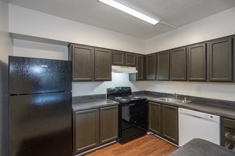 A black refrigerator sits in a kitchen with brown cabinets.