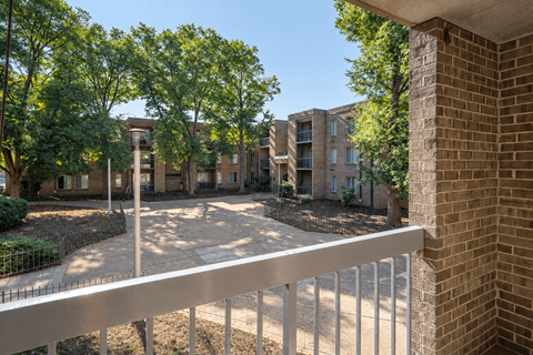 A view of a courtyard from a balcony with trees and buildings in the background.