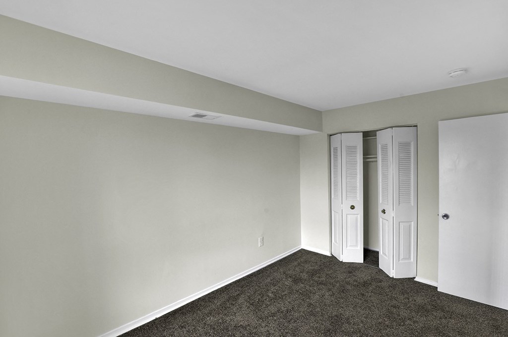 a bedroom with white walls and carpet and two closet doors