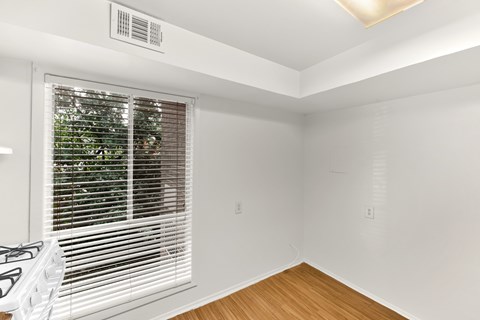 A room with a window covered by white blinds and a white gas stove.