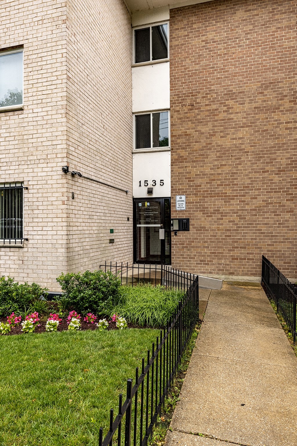 the front of a brick building with a sidewalk and grass