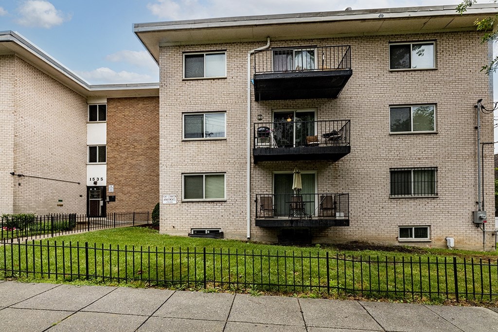 a brick apartment building with two balconies and a green lawn