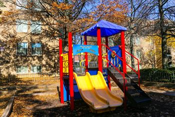 a playground with slides and a swing set in front of an apartment building