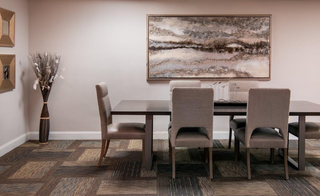 A brown dining table with four chairs and a vase with dried flowers.
