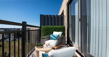 A balcony with a table, chairs, and a potted plant.