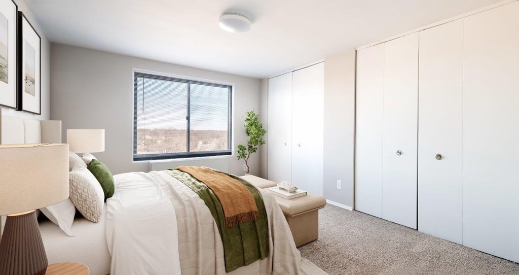 A bedroom with a bed, a lamp, a window, and a plant.