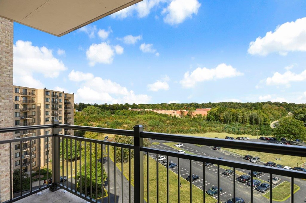 A balcony overlooks a parking lot and greenery.