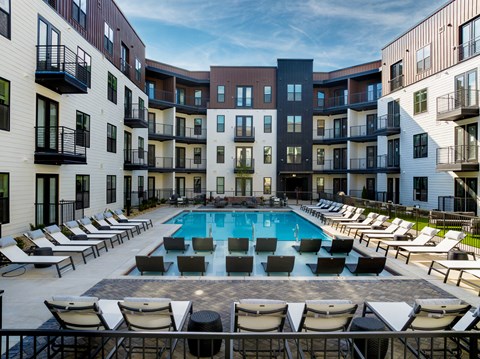 A swimming pool surrounded by lounge chairs in front of apartment buildings.