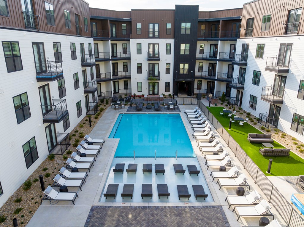 A large swimming pool surrounded by sun loungers and balconies of apartment buildings.