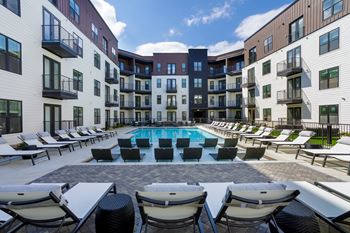 A large swimming pool surrounded by lounge chairs in front of apartment buildings.