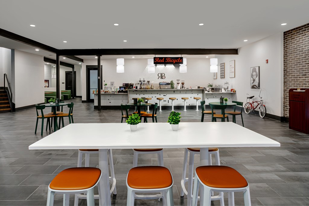 A white table with orange chairs is in the foreground of a room with a bar in the background.