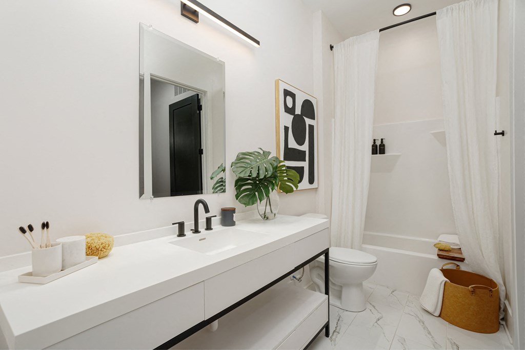 A white bathroom with a sink, mirror, toilet, and a plant at Vintage Edge Nashville Apartments, Nashville, TN