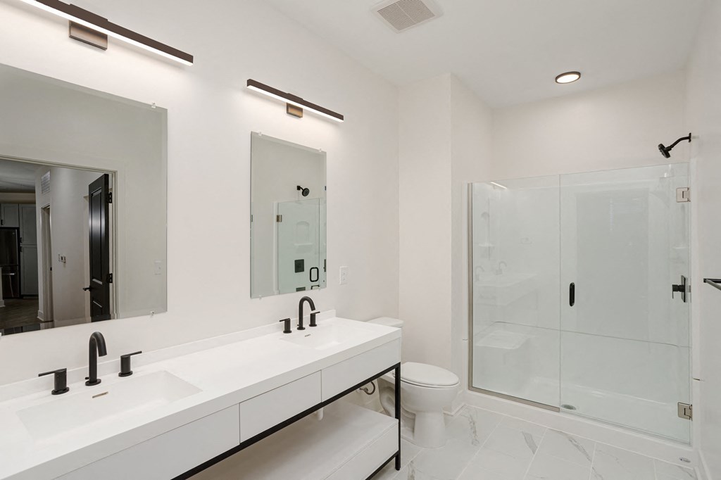 A white bathroom with a sink, mirror, toilet, and shower at Vintage Edge Nashville Apartments, Tennessee, 37211