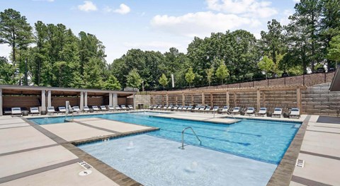 A large outdoor swimming pool surrounded by lounge chairs and trees at Vintage Raleigh West Apartments, Raleigh