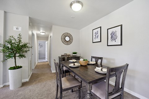 A dining room with a table set for two and a plant in a white pot.