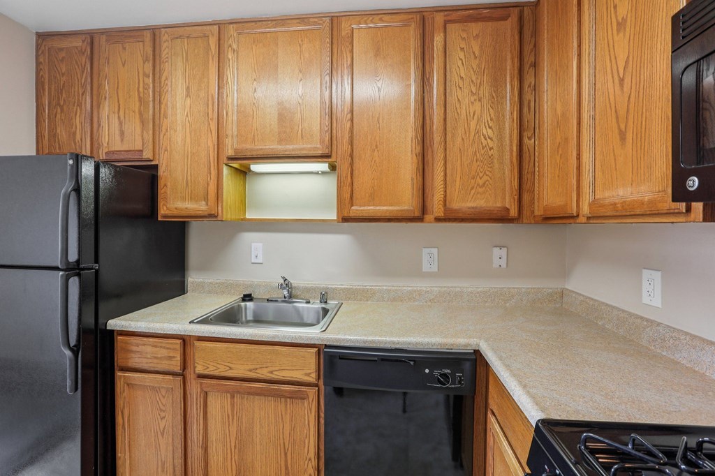 A kitchen with wooden cabinets and a black refrigerator.