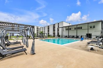 A pool area with sun loungers and a building in the background.